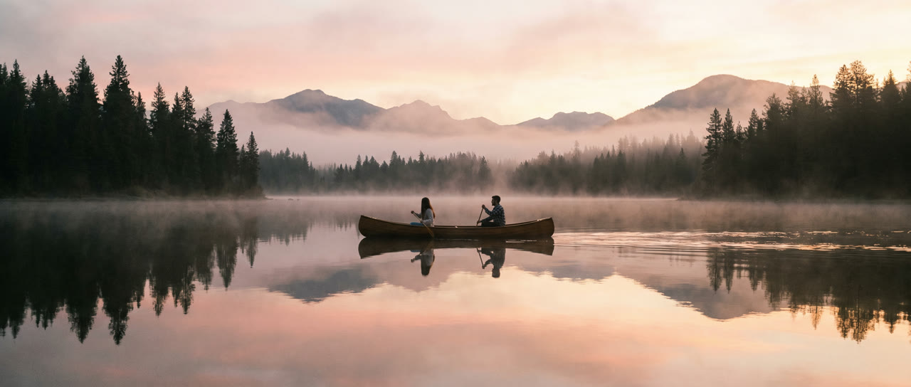 Paar im Kanu auf einem nebligen See bei Sonnenaufgang